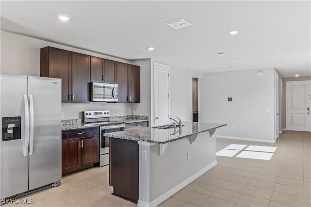 kitchen featuring stone counters, a sink, visible vents, appliances with stainless steel finishes, and an island with sink