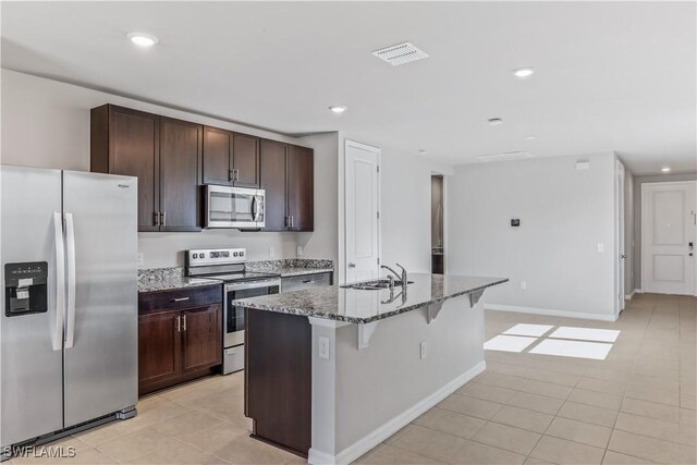 kitchen with appliances with stainless steel finishes, a sink, stone counters, an island with sink, and a breakfast bar