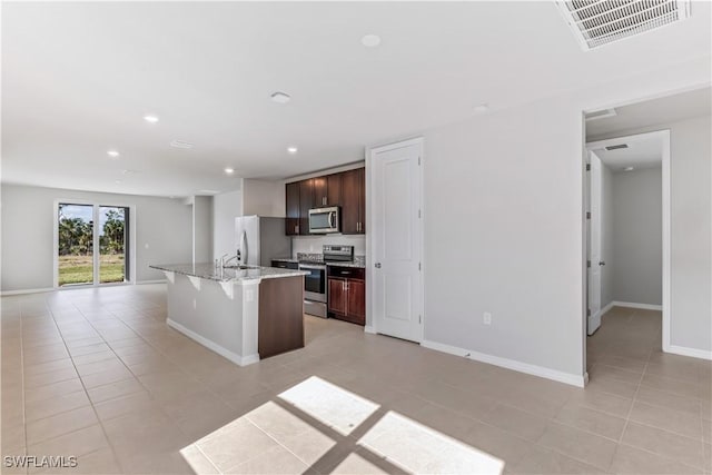 kitchen featuring visible vents, an island with sink, appliances with stainless steel finishes, open floor plan, and a kitchen breakfast bar