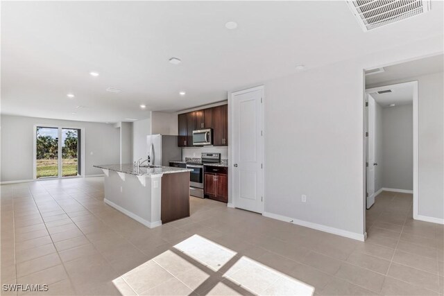 kitchen with appliances with stainless steel finishes, open floor plan, light tile patterned flooring, a kitchen breakfast bar, and an island with sink