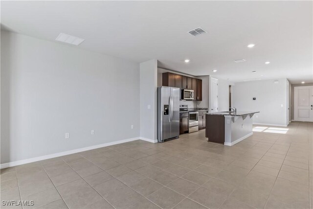 kitchen featuring stainless steel appliances, a breakfast bar, light tile patterned floors, a center island with sink, and open floor plan