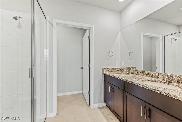 bathroom featuring a stall shower, double vanity, tile patterned flooring, and baseboards