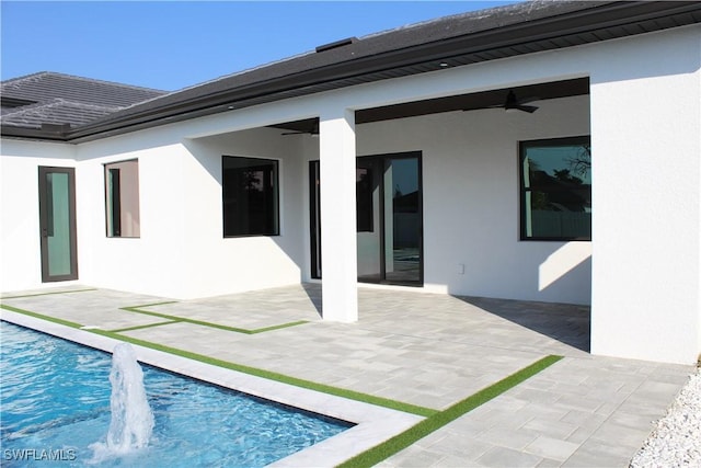 back of property with an outdoor pool, a ceiling fan, and stucco siding