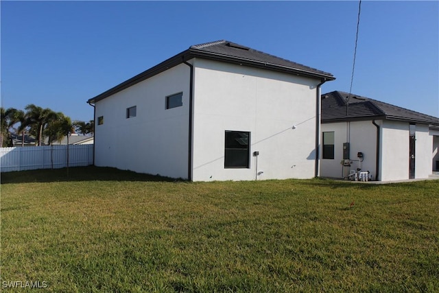 rear view of property featuring a lawn, fence, and stucco siding