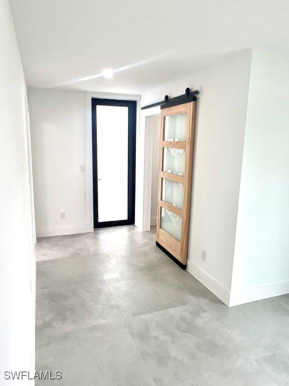 spare room featuring concrete flooring, a barn door, and baseboards