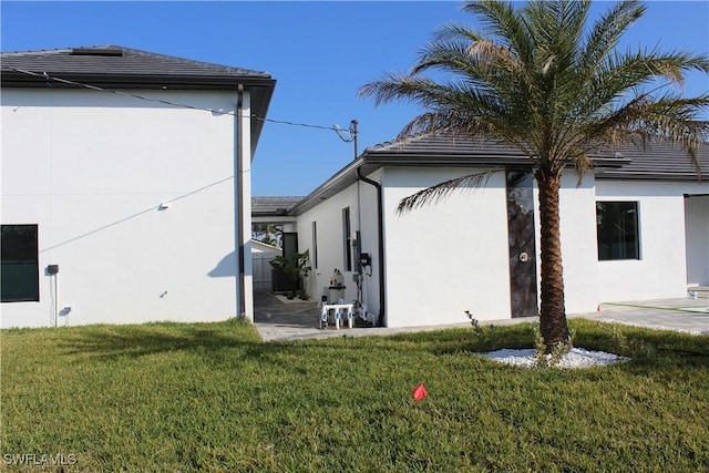 view of side of home with a yard, a patio, and stucco siding