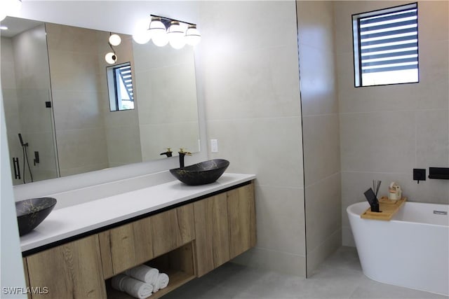 bathroom featuring tile walls, double vanity, a freestanding bath, a sink, and a shower stall