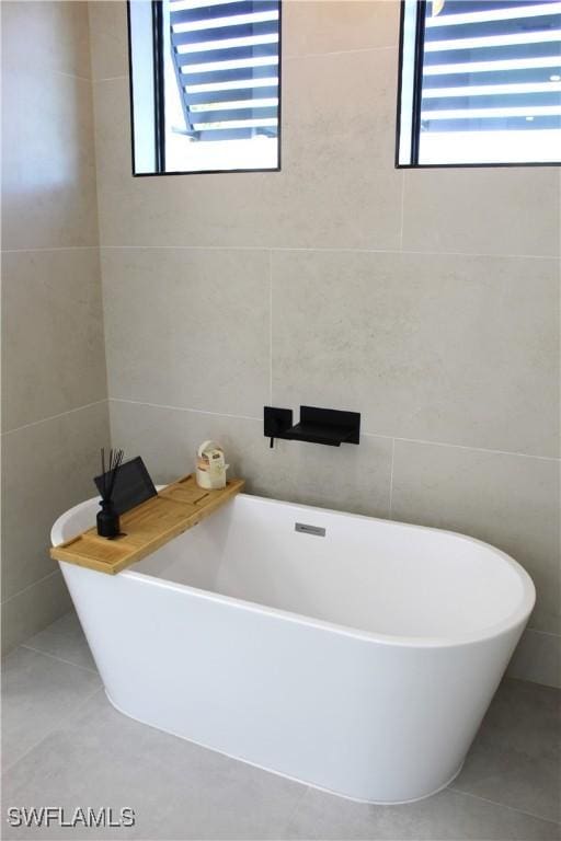 full bath featuring a freestanding tub, a healthy amount of sunlight, and tile walls