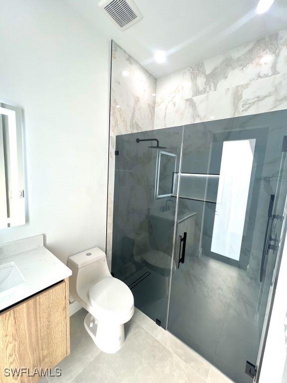 bathroom featuring tile patterned flooring, toilet, vanity, visible vents, and a shower stall