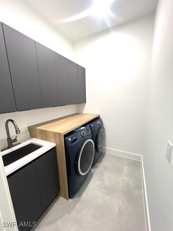 clothes washing area featuring washer and dryer, cabinet space, a sink, and baseboards