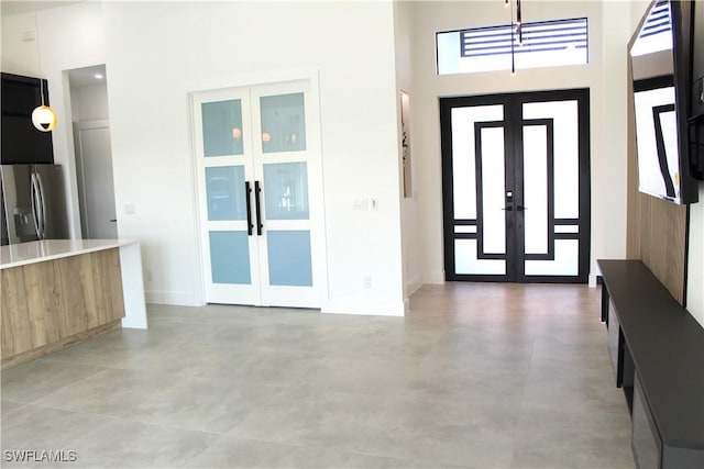 foyer with french doors, a towering ceiling, and baseboards