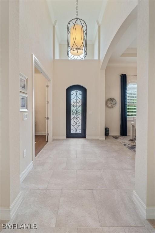 entrance foyer with ornamental molding, arched walkways, a chandelier, and baseboards