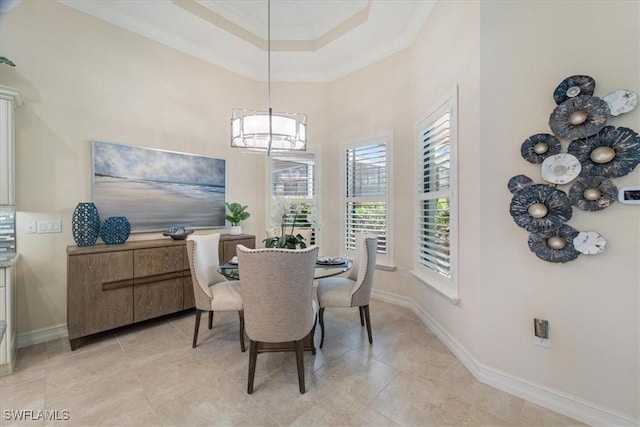 dining space with light tile patterned flooring, a high ceiling, baseboards, ornamental molding, and a raised ceiling