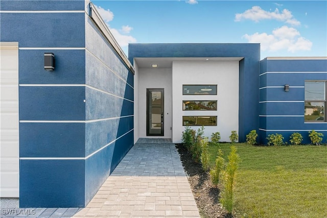 doorway to property featuring an attached garage, a lawn, and stucco siding