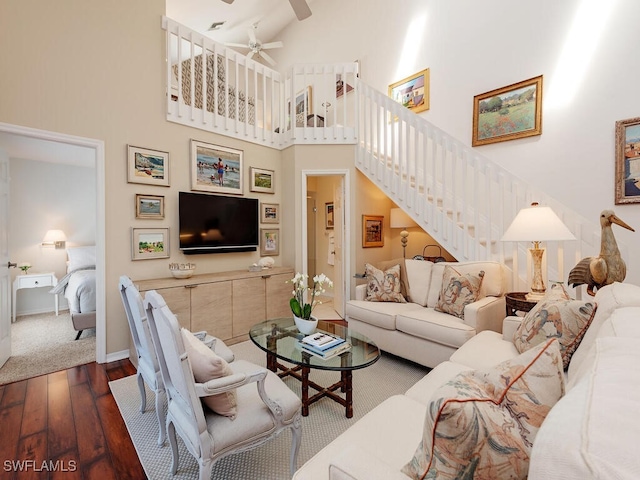 living area featuring baseboards, a towering ceiling, ceiling fan, dark wood-type flooring, and stairs