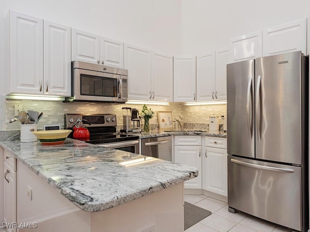 kitchen featuring light tile patterned floors, stainless steel appliances, a sink, white cabinets, and light stone countertops