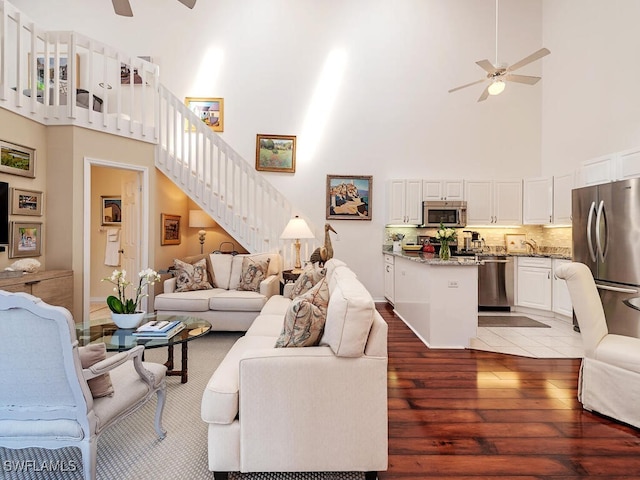 living room with a ceiling fan, stairway, a towering ceiling, and wood finished floors