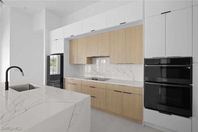 kitchen featuring modern cabinets, white cabinetry, a sink, light stone countertops, and black appliances