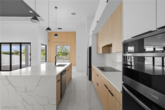 kitchen featuring light stone counters, hanging light fixtures, modern cabinets, a large island with sink, and black appliances