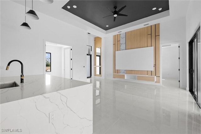 kitchen featuring marble finish floor, a raised ceiling, hanging light fixtures, a sink, and light stone countertops