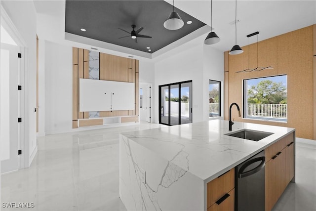 kitchen featuring light stone counters, a kitchen island with sink, a tray ceiling, modern cabinets, and decorative light fixtures