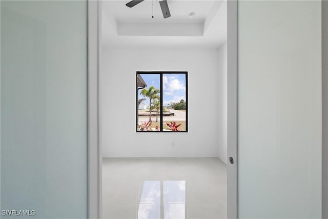 empty room with ceiling fan and a raised ceiling