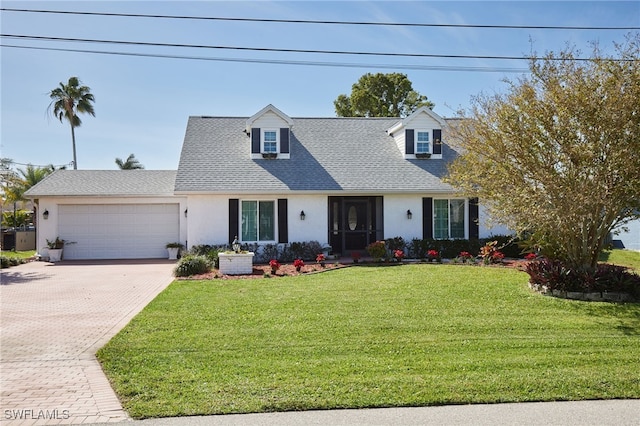 cape cod home with decorative driveway, roof with shingles, stucco siding, an attached garage, and a front lawn