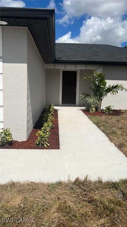 view of exterior entry with roof with shingles and stucco siding