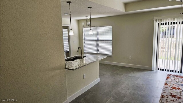 1125 Copley St E, Lehigh Acres, FL 33974 - kitchen with healthy amount of natural light, a sink, baseboards, hanging light fixtures, and a textured wall