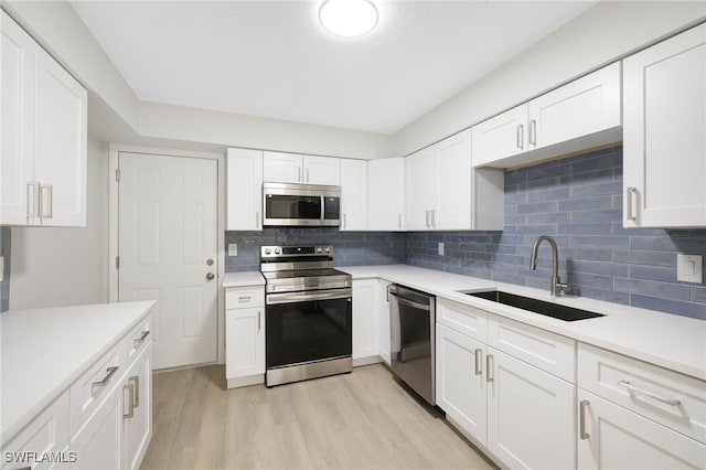 kitchen with light wood-style flooring, a sink, white cabinets, light countertops, and appliances with stainless steel finishes