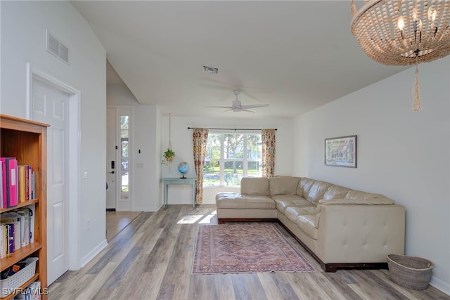 living room featuring ceiling fan with notable chandelier, wood finished floors, visible vents, and baseboards