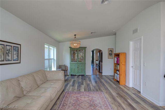 living room featuring visible vents, arched walkways, vaulted ceiling, and wood finished floors