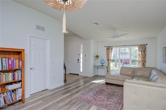 living room with vaulted ceiling, light wood finished floors, ceiling fan with notable chandelier, and visible vents