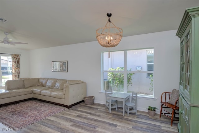 living area with light wood finished floors, visible vents, baseboards, and ceiling fan with notable chandelier