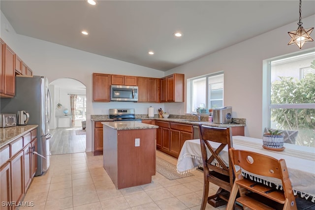 kitchen with arched walkways, a kitchen island, hanging light fixtures, appliances with stainless steel finishes, and light stone countertops