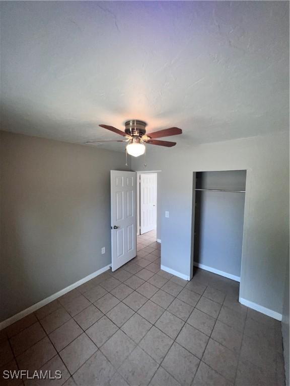 unfurnished bedroom with a closet, ceiling fan, baseboards, and light tile patterned floors