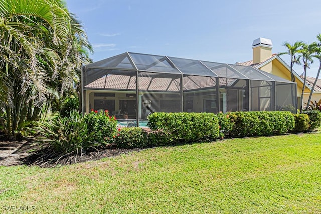 rear view of property with a yard, a chimney, and a lanai