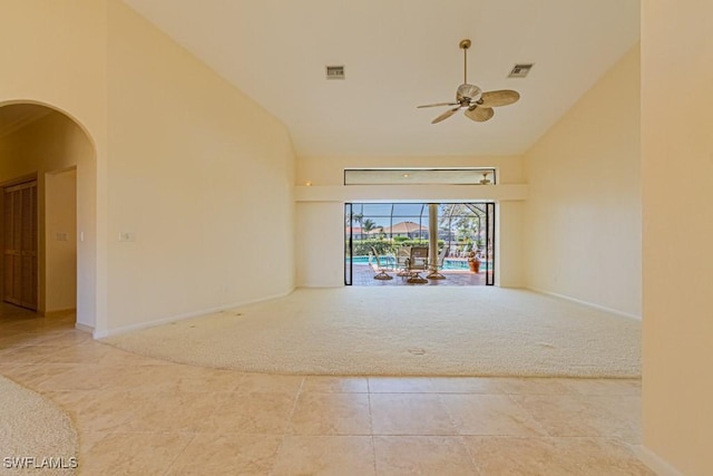 tiled spare room with carpet floors, arched walkways, visible vents, and high vaulted ceiling