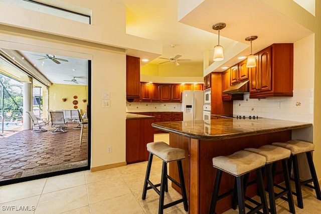 kitchen featuring white appliances, tasteful backsplash, light tile patterned floors, a peninsula, and under cabinet range hood