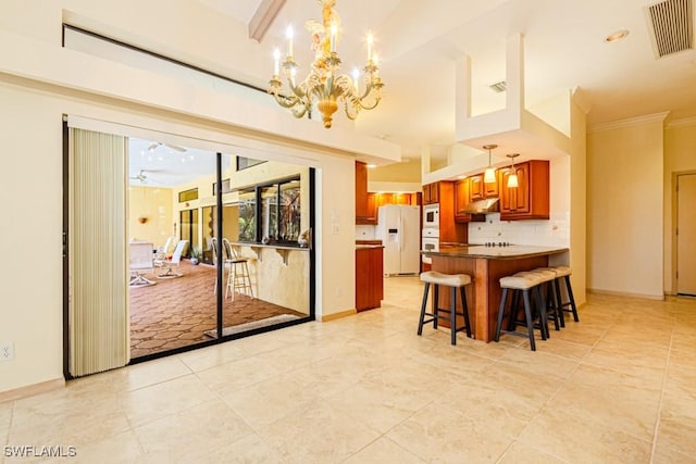 kitchen featuring under cabinet range hood, white appliances, visible vents, tasteful backsplash, and brown cabinetry