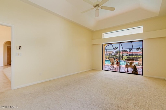 carpeted empty room with arched walkways, a raised ceiling, ceiling fan, and baseboards