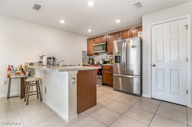 kitchen featuring stainless steel appliances, brown cabinets, visible vents, and decorative backsplash