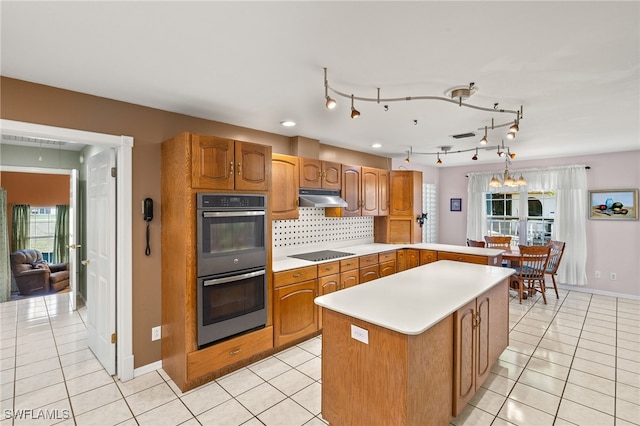 kitchen with backsplash, black electric stovetop, under cabinet range hood, double oven, and light tile patterned flooring