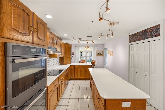 kitchen with stainless steel double oven, light countertops, under cabinet range hood, black electric stovetop, and a center island