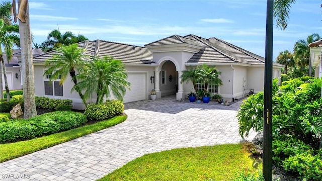 single story home featuring a garage, decorative driveway, a tile roof, and stucco siding