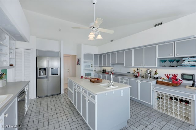 kitchen featuring stainless steel appliances, a sink, light countertops, open shelves, and a center island with sink