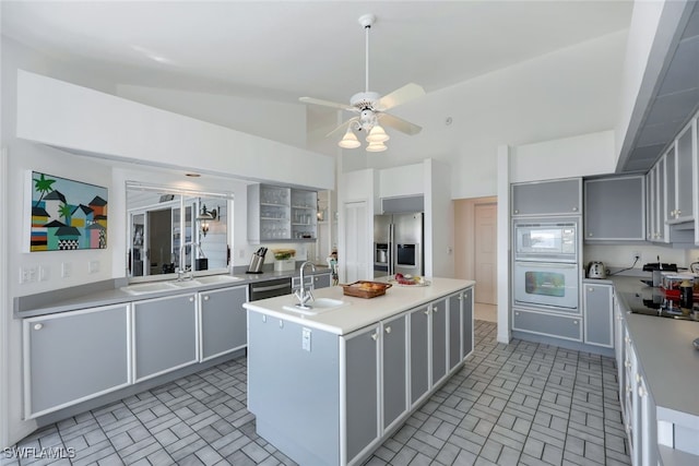 kitchen featuring light countertops, gray cabinets, a kitchen island with sink, and stainless steel refrigerator with ice dispenser