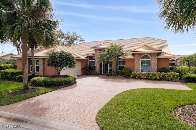 view of front of property featuring a garage, a tile roof, decorative driveway, and a front yard