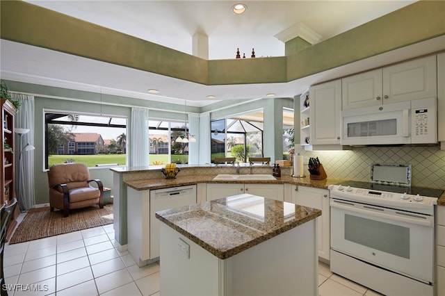 kitchen featuring a peninsula, white appliances, light stone counters, and a center island