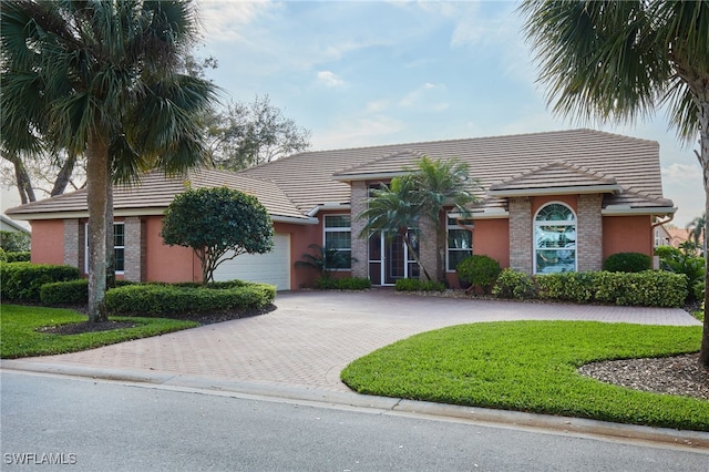 ranch-style house with a garage, decorative driveway, a tile roof, and stucco siding